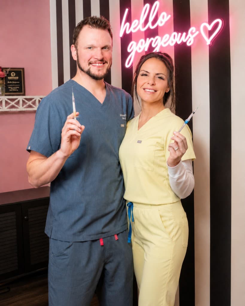 Danielle Alcala-Glazier and Ryan Kent, FNP-BC at Hello Gorgeous Med Spa in Oswego, IL — founders with the hello gorgeous neon sign